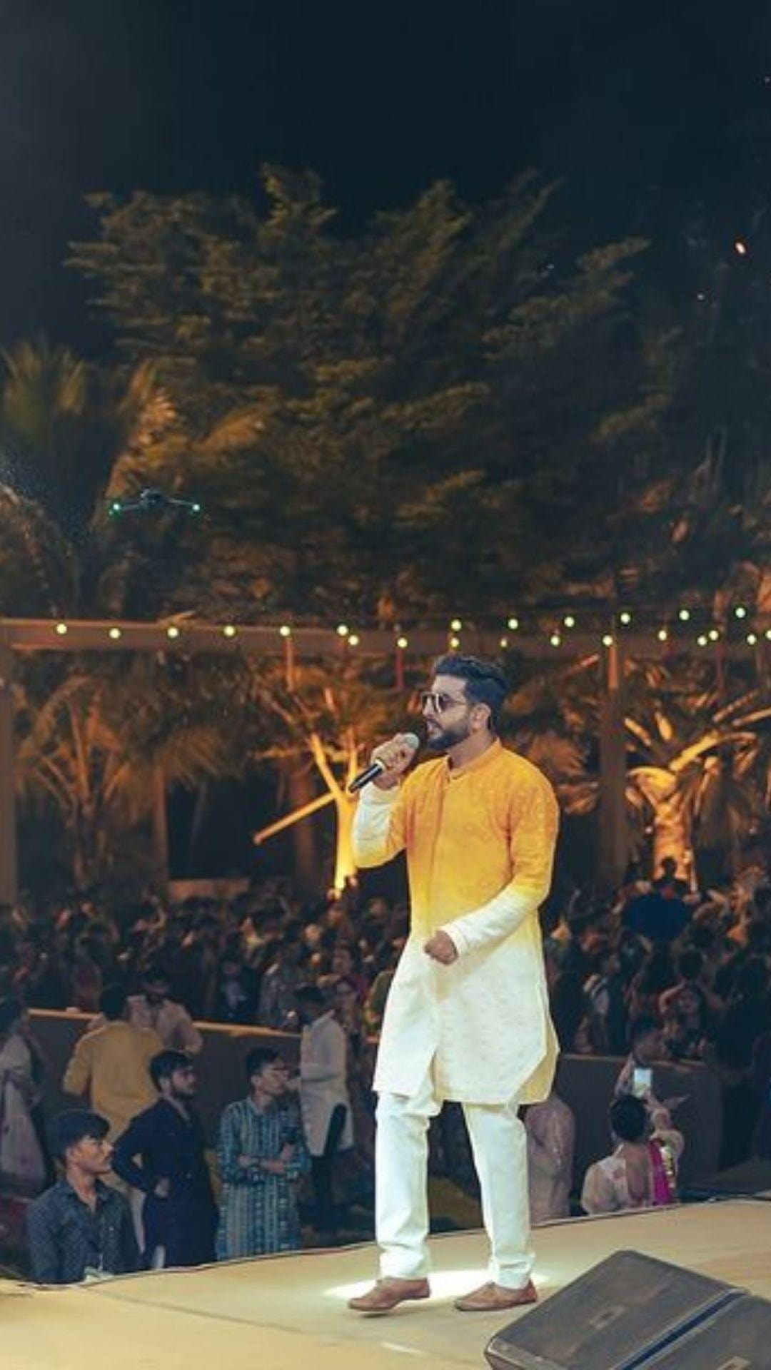 Jigardan Gadhavi singing on a long stage in front of a packed Navratri ground strung with festoon lights
