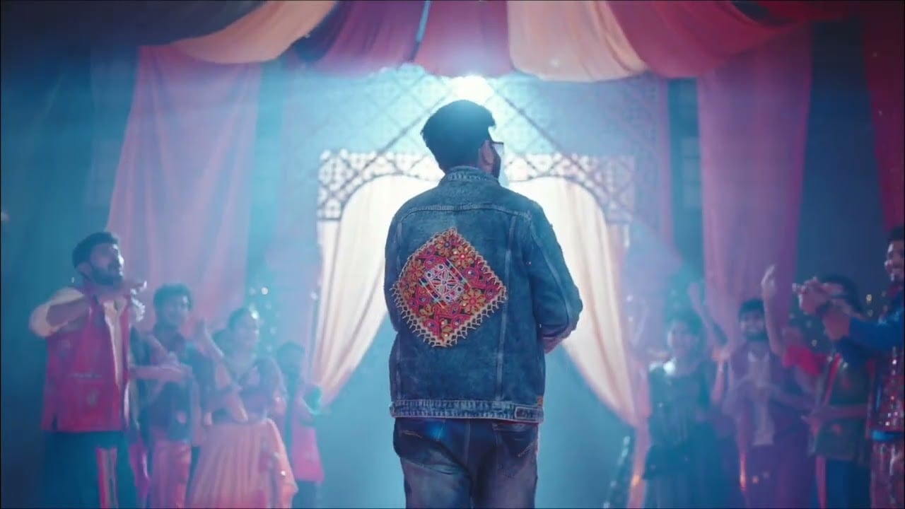 Jigardan Gadhavi walking towards a lit garba stage in a Kutch mirror-work denim jacket