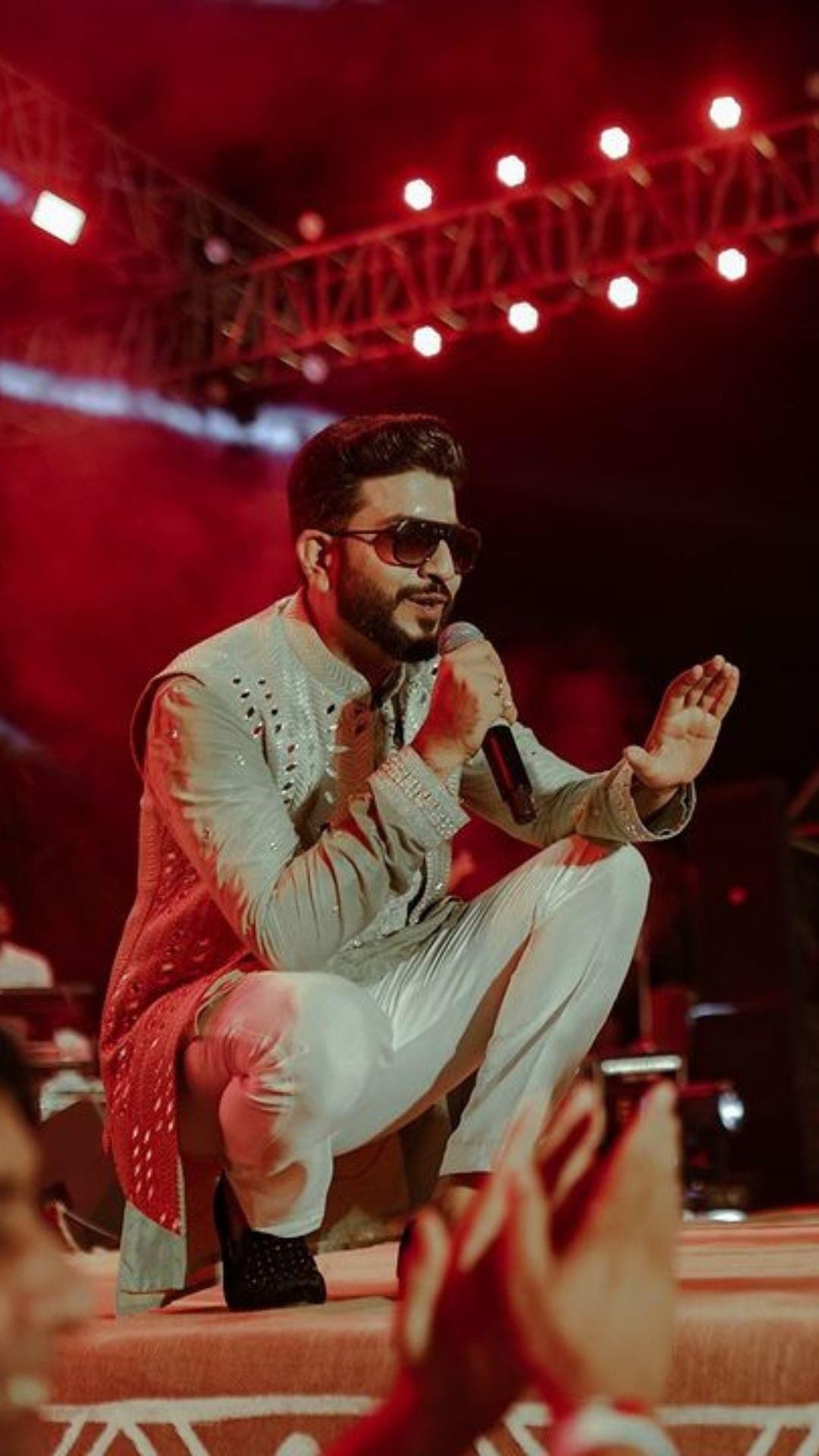 Jigardan Gadhavi crouched at the edge of the stage under red lights, reaching towards the crowd