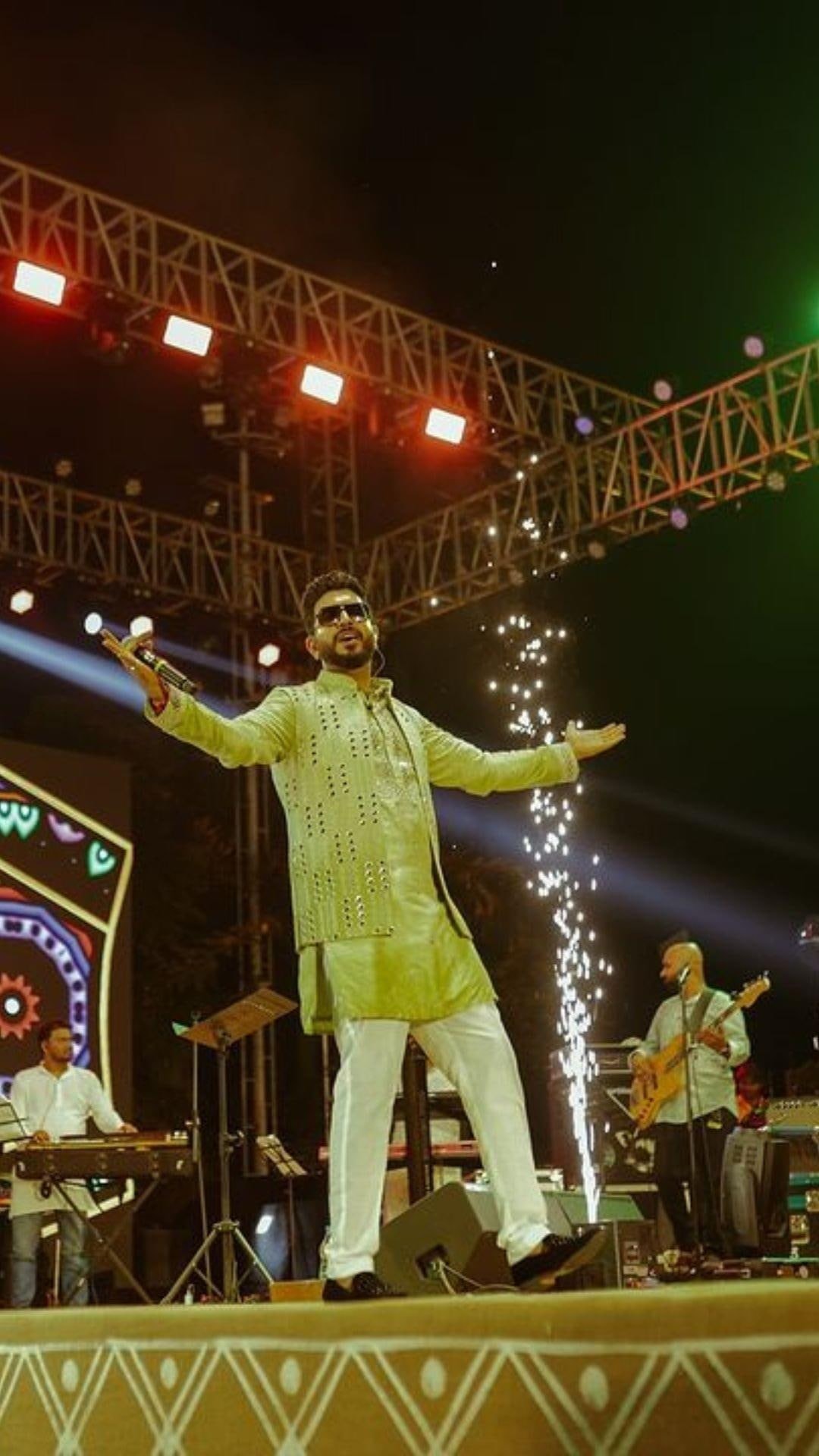 Jigardan Gadhavi on stage with his arms wide, sparks firing behind him